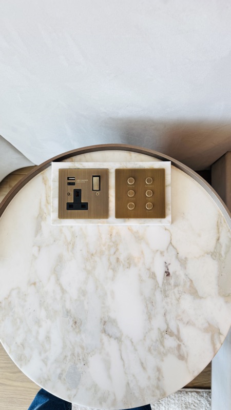 A brass-finish scene keypad alongside bedside power and charging connections.