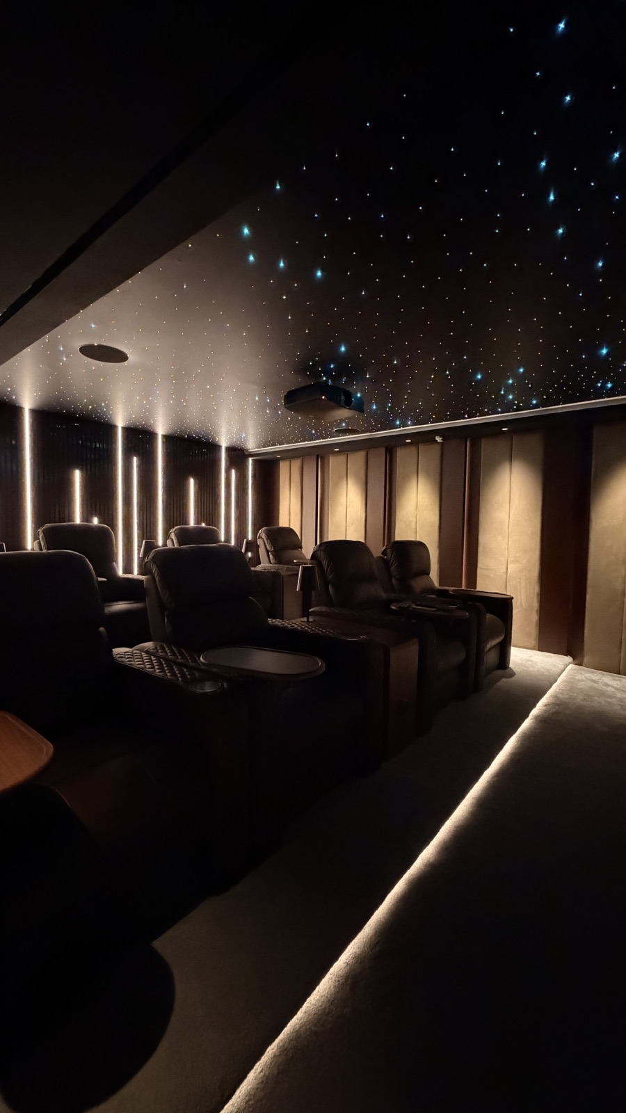 Reclining cinema seats beneath a star ceiling, with illuminated aisles and wall lighting.