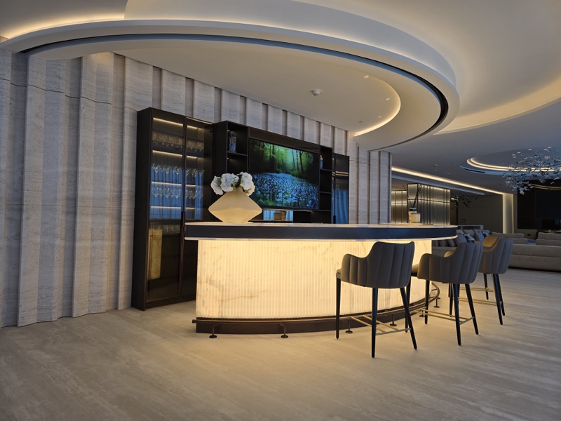 A home bar and entertainment space with a television, illuminated shelving and curved ceiling lighting.