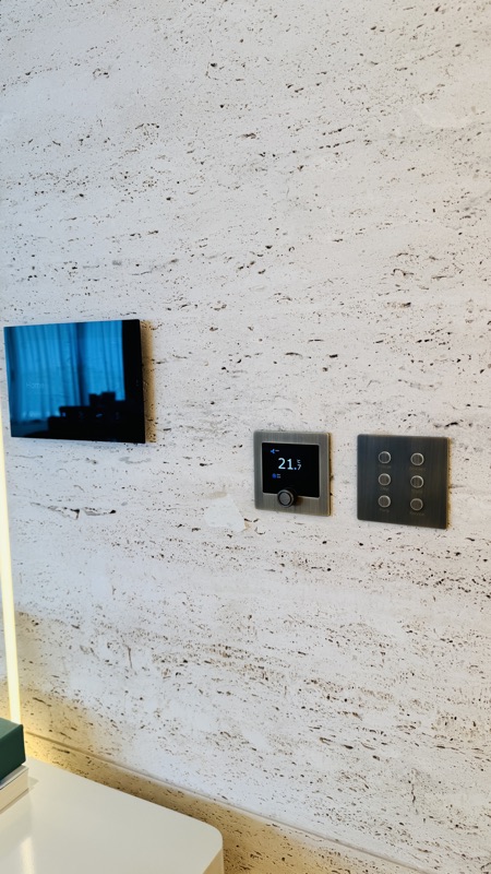 A touchscreen, thermostat and scene keypad grouped within a stone wall finish.